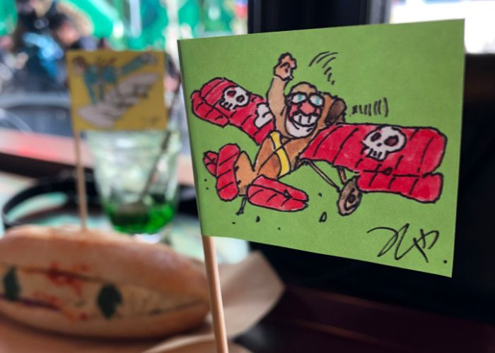 A flag with an illustration of a man in a red plane with skulls on the wings, stuck into a sandwich.